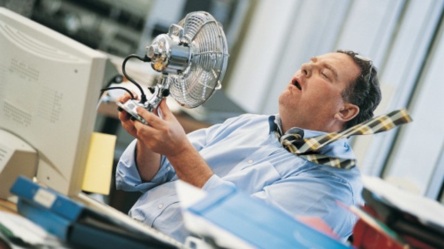 Büromitarbeiter hält sich einen Ventilator vor das Gesicht